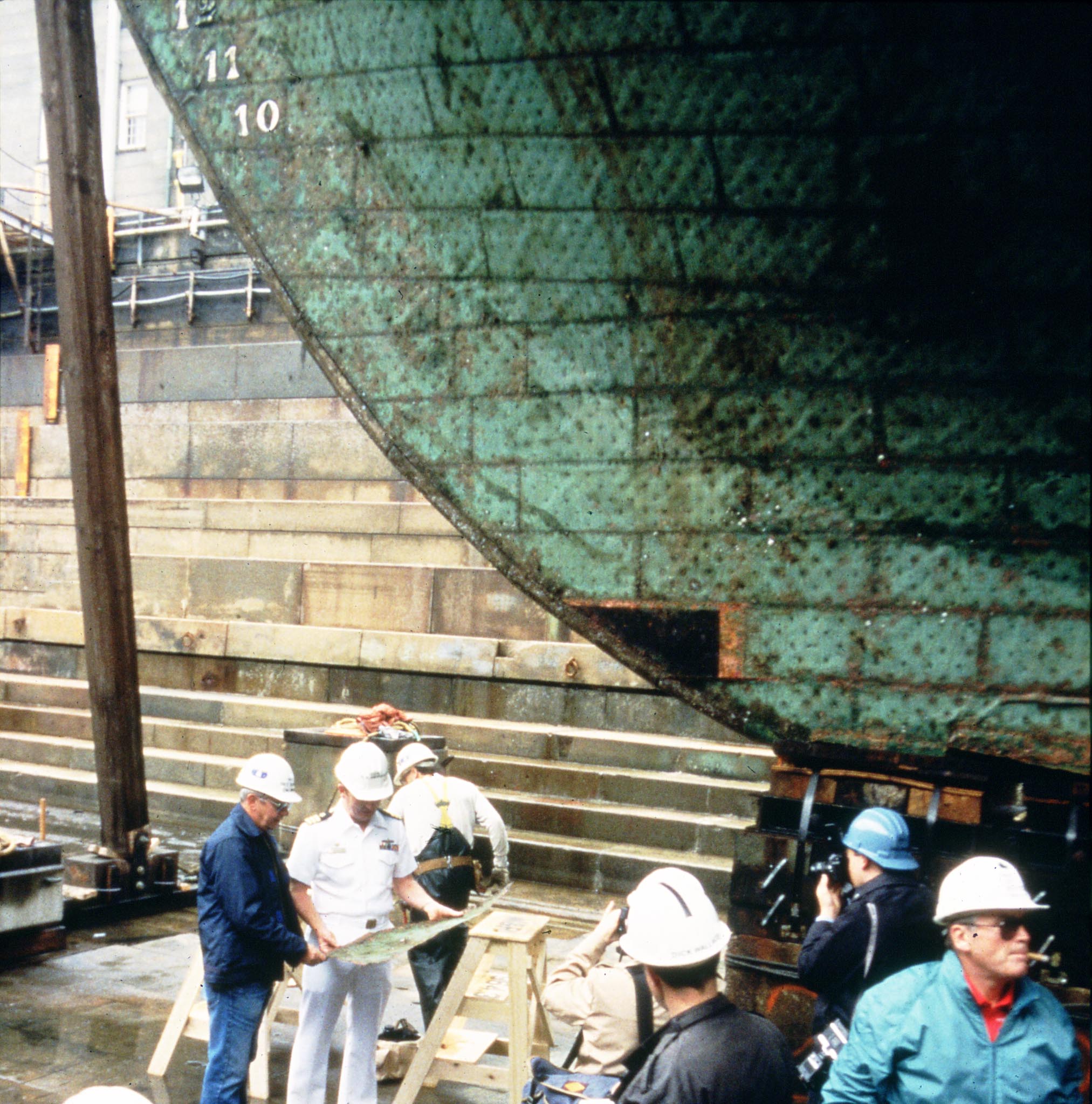 CDR Richard Bradford Amirault, in white uniform, removing the first piece of copper from Constitution's hull, 1992. [Courtesy Naval History & Heritage Command Detachment Boston]
