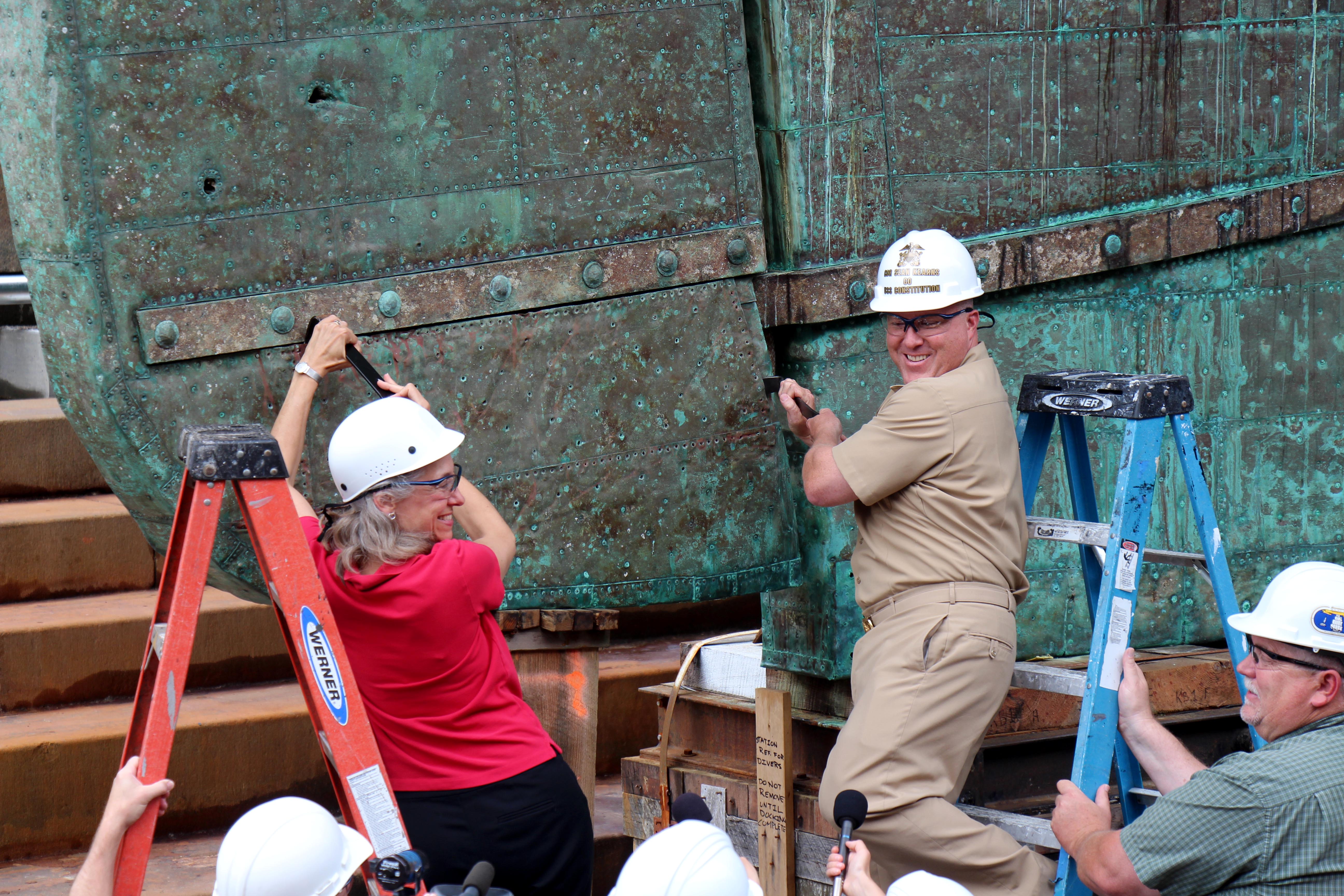 CDR Sean Kearns and USS Constitution Museum President Anne Grimes Rand remove the first sheet of copper for the ship, June 9, 2015. [Courtesy USS Constitution Museum]