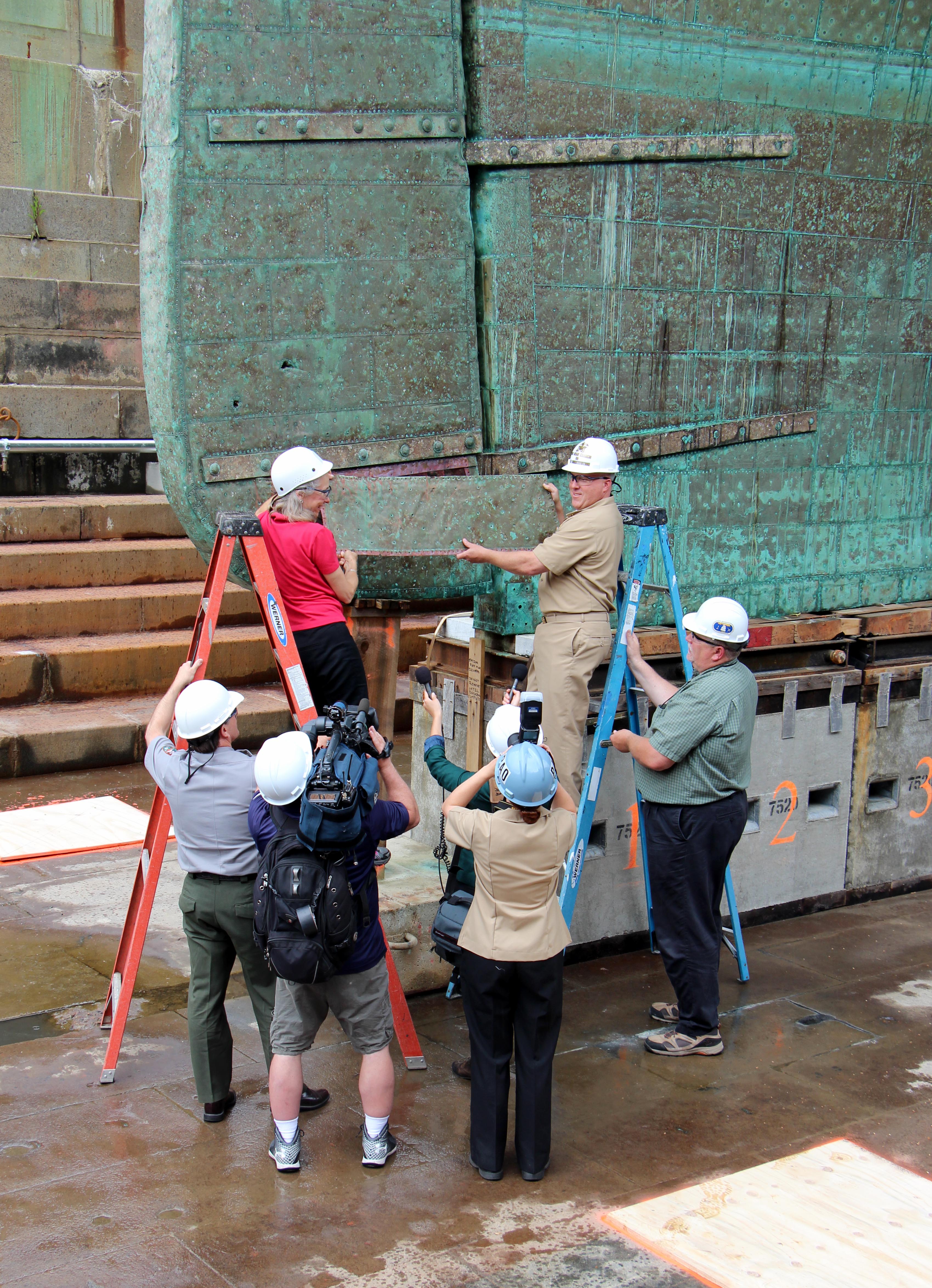 CDR Sean Kearns and USS Constitution Museum President Anne Grimes Rand ceremoniously remove the first sheet of copper on June 9, 2015. [Courtesy USS Constitution Museum]