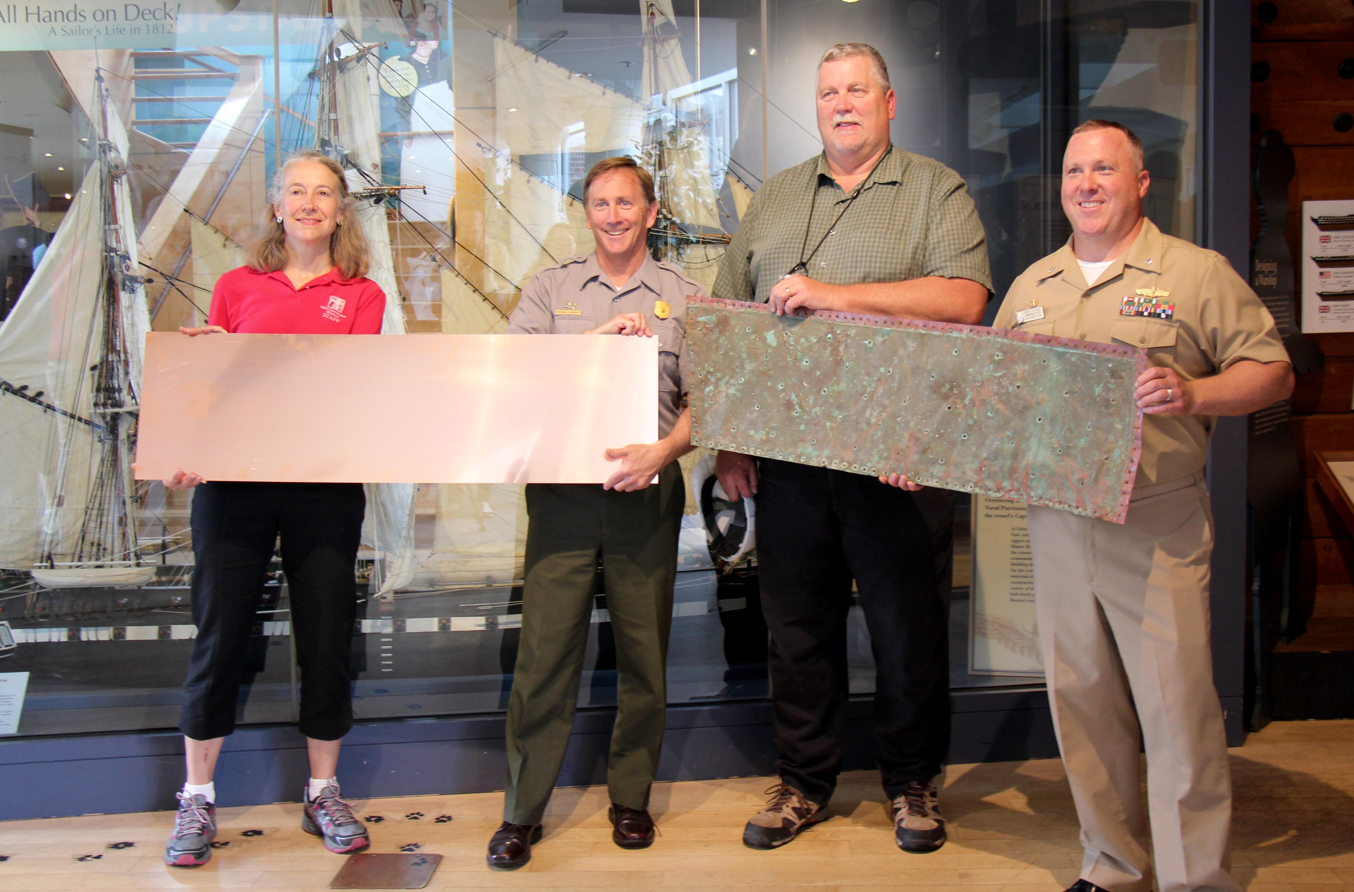USS Constitution Museum President Anne Grimes Rand, Superintendent for the National Parks of Boston Michael Creasey, Boston Naval History & Heritage Command Detachment Boston Director Richard Moore, and USS Constitution Commanding Officer Sean Kearns, pose with new and old copper sheets in the USS Constitution Museum on June 9, 2015. [Courtesy USS Constitution Museum]