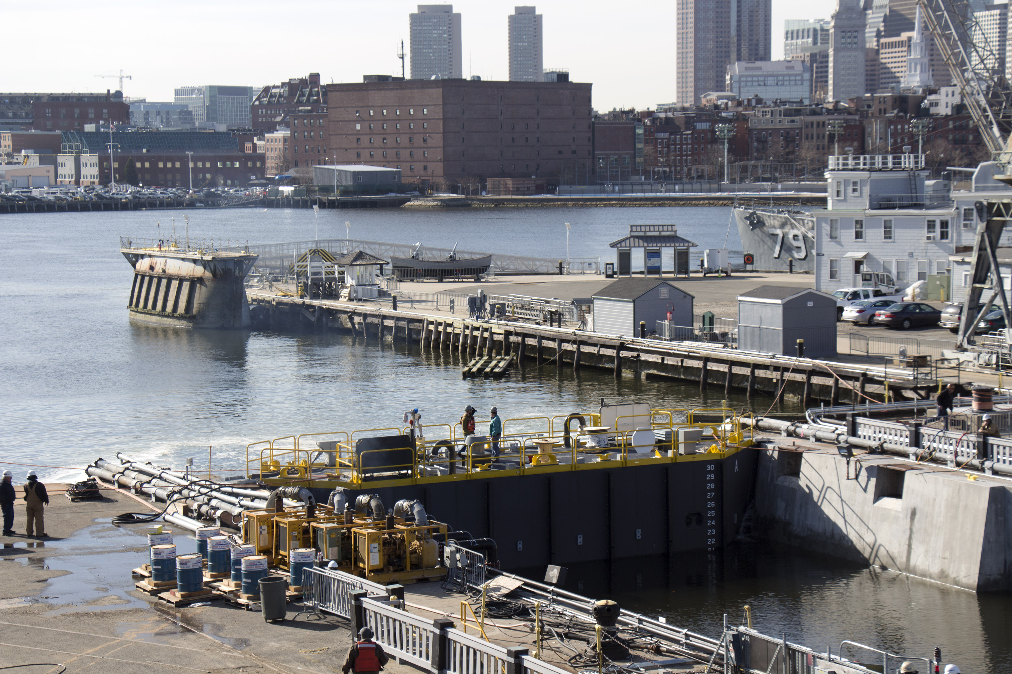 The new steel caisson is installed for testing in April 2015. The former caisson is tied up along the pier in the background. [Courtesy USS Constitution Museum]