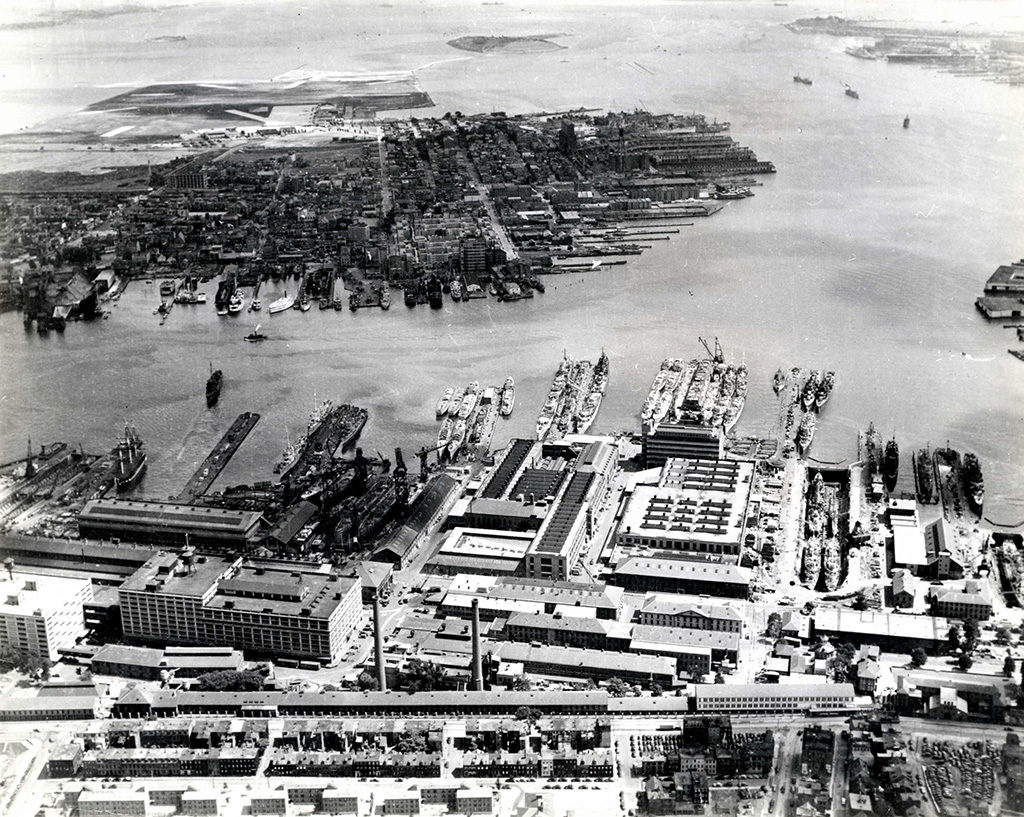 Aerial view of Boston Navy Yard, Boston, Massachusetts, in 1942. The Navy Yard is nearly at its full force of 50,000 workers, principally repairing warships damaged in battle. Can you spot USS Constitution amidst the piers and U.S. Navy vessels? Note the flat landscape in the top of the photo, known as Jeffrey Field (now Logan International Airport). [Courtesy of the National Archives and Records Administration, ARC 7329867]
