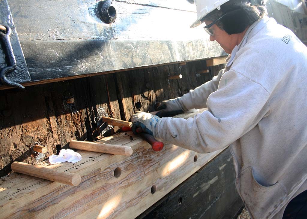 NHHC ship restorer Anita Petricone drives oak plugs into holes left behind after a hull plank and its fasteners have been removed. [Courtesy Naval History & Heritage Command Detachment Boston]