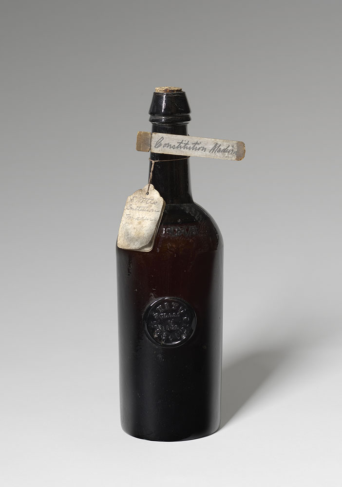 Corked glass bottle with a wooden tag that reads "Constitution Madeira"