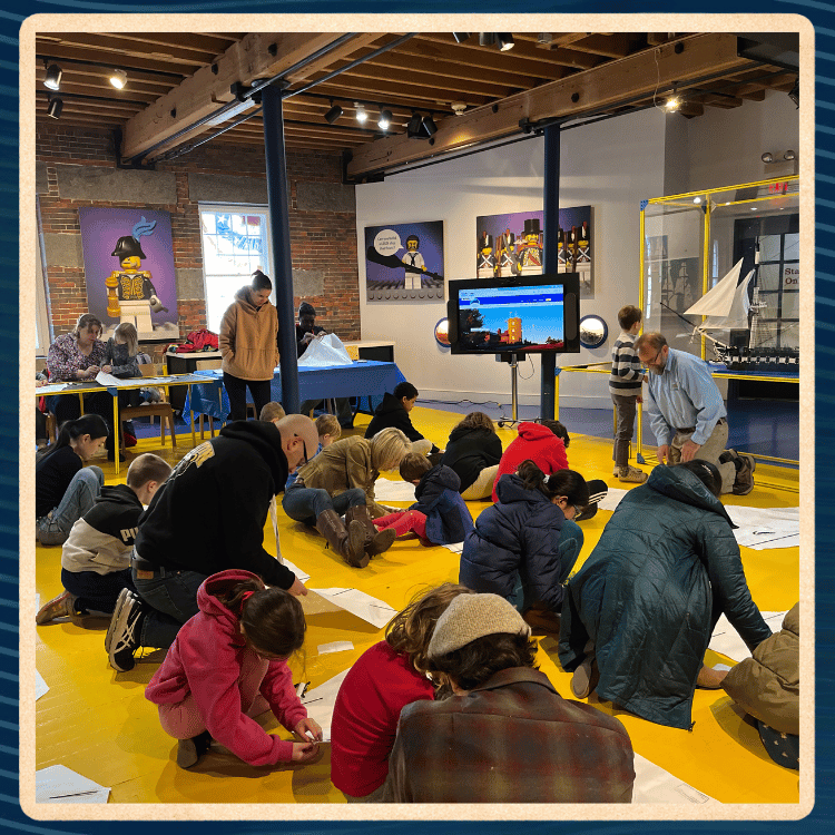 People of all ages sit on the floor of a museum making kites.