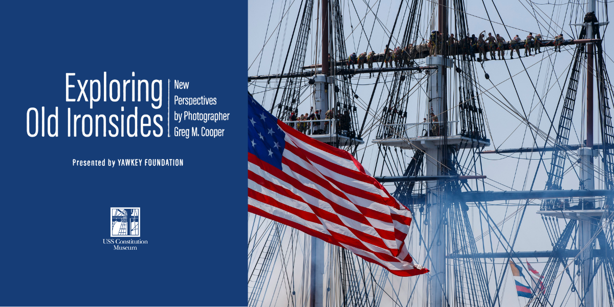 image of frigate mast, with sailors, and the american flag flying.