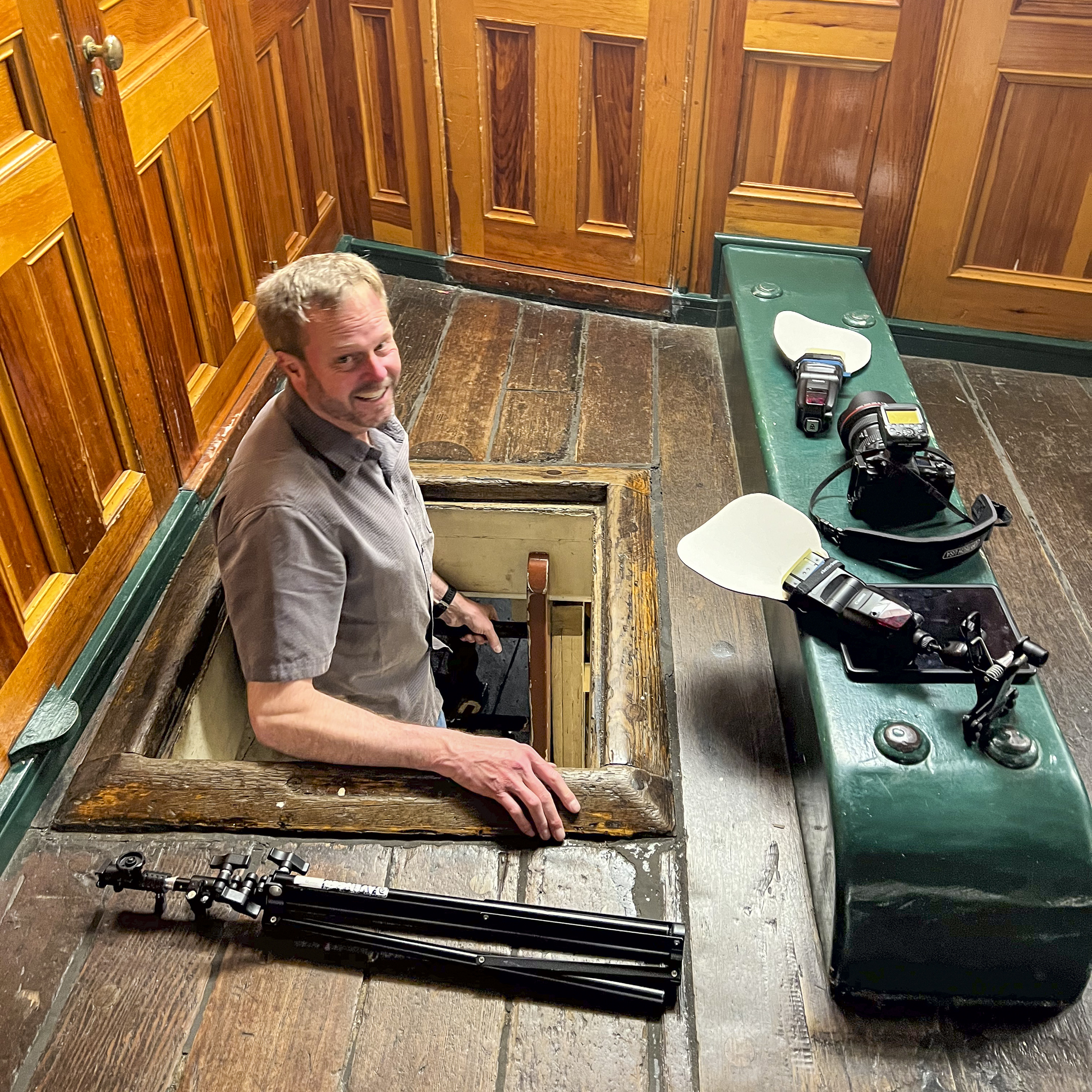 Man emerging from a hole in ship floor, surrounded by camera equipment
