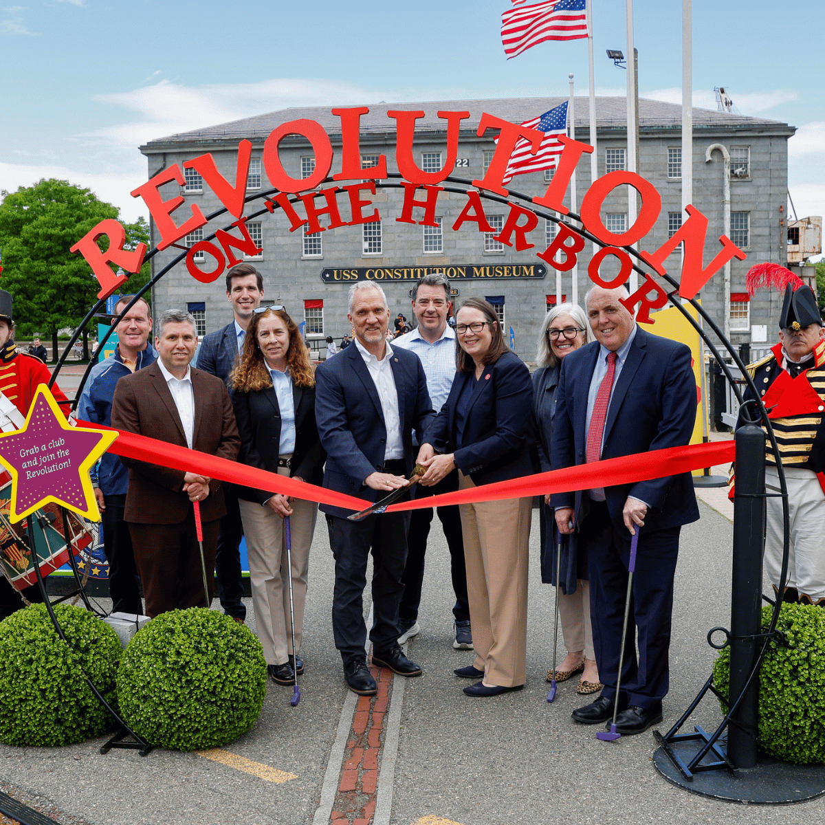 A group of 8 people pose while cutting a ribbon for a new mini golf course at Museum.